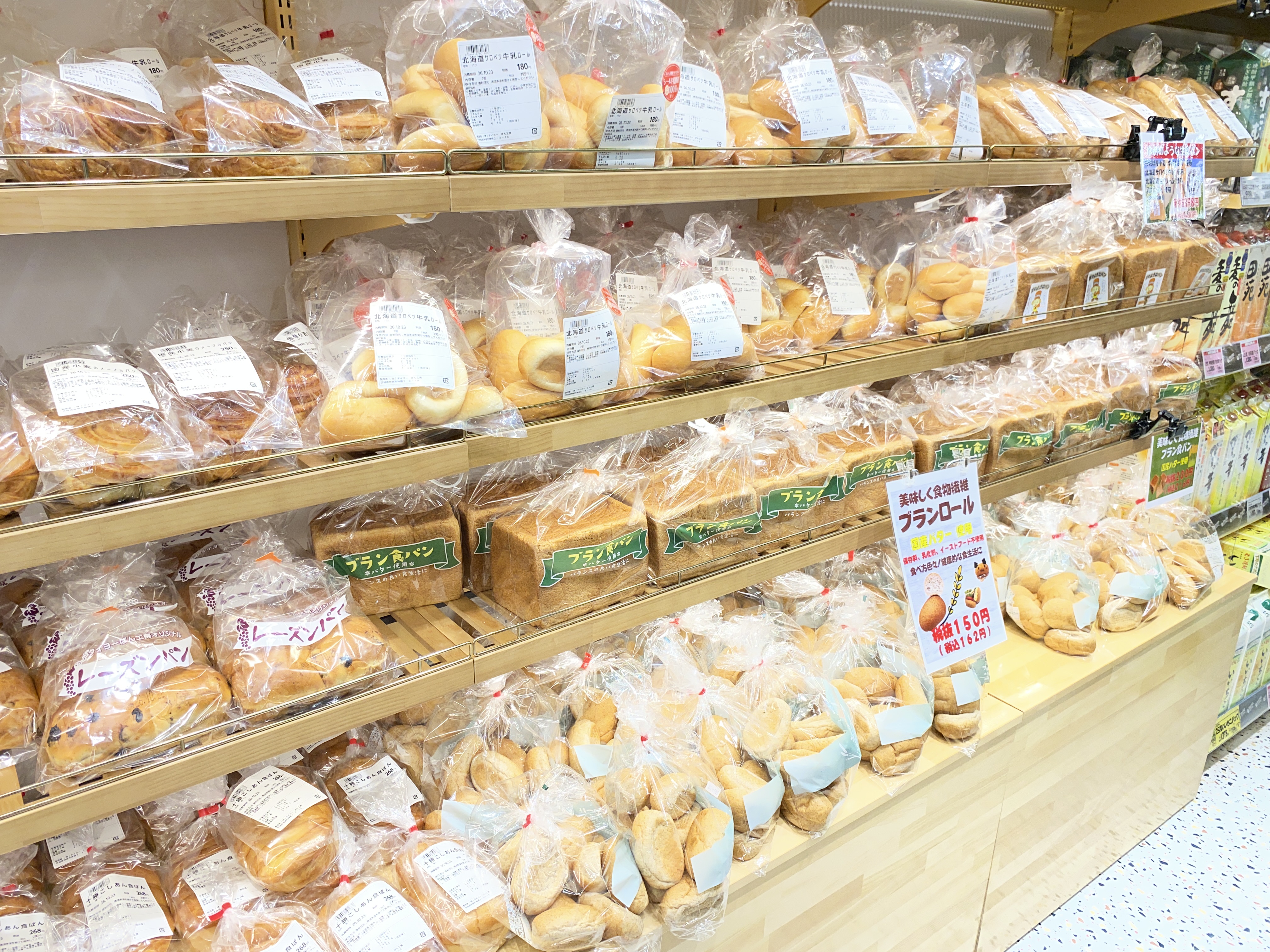袋入りの食パンやロールパンが並ぶベーカリーの棚